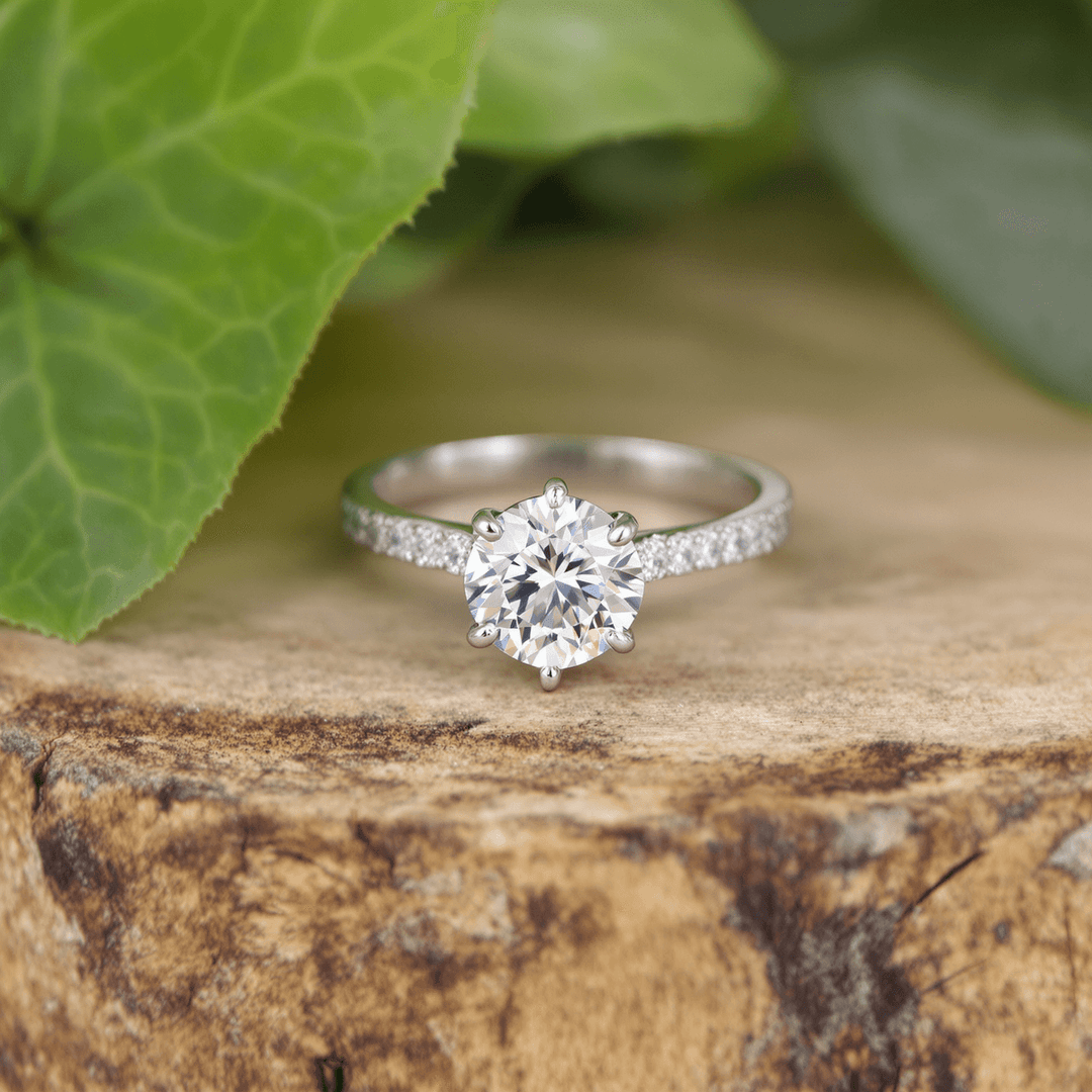 Close-up of a sparkling lab-grown diamond engagement ring on wood, surrounded by green leaves symbolizing sustainability and ethical sourcing.