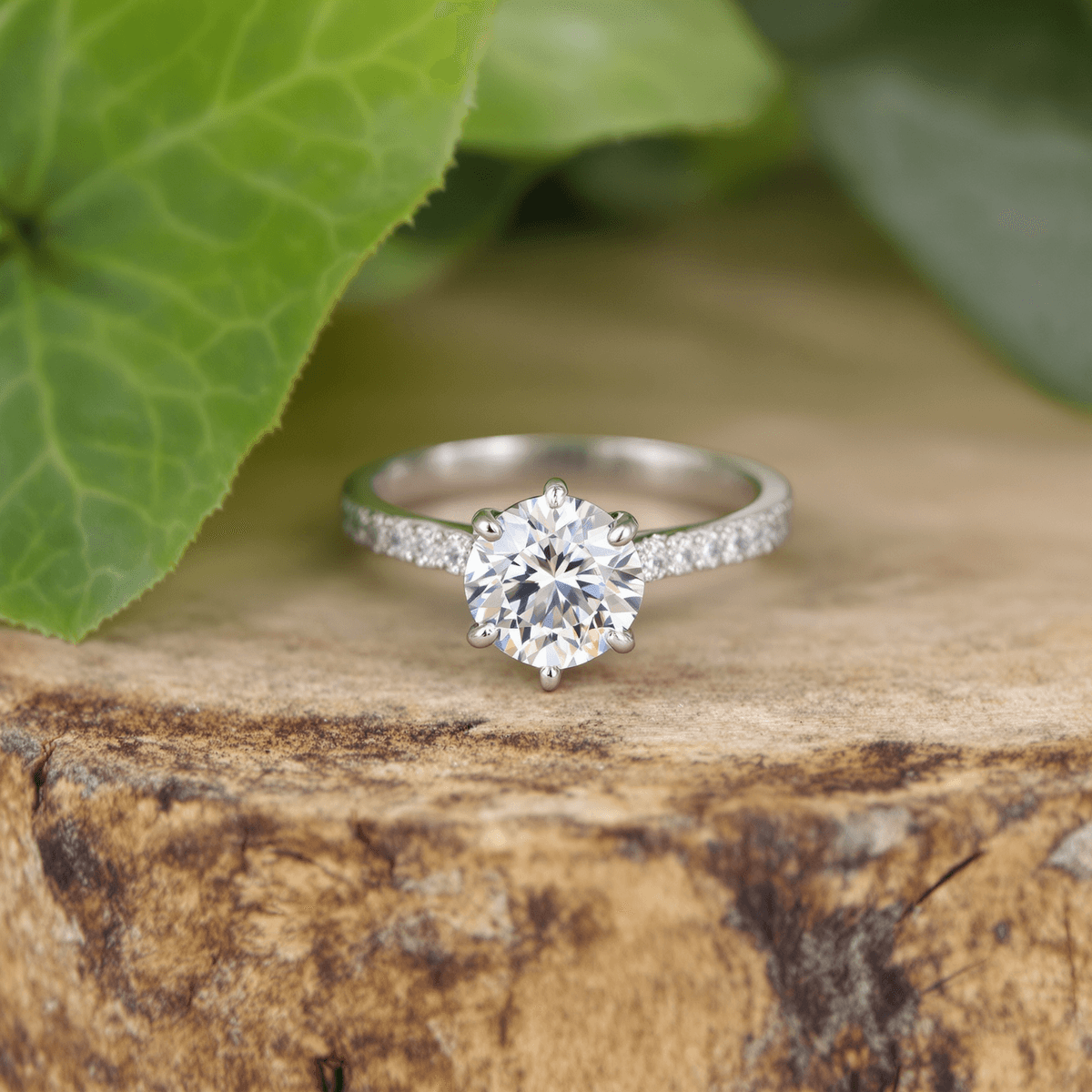 Close-up of a sparkling lab-grown diamond engagement ring on wood, surrounded by green leaves symbolizing sustainability and ethical sourcing.