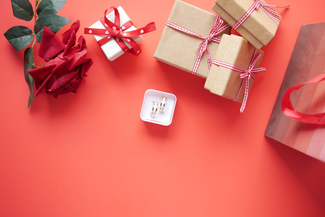 Valentines day gift box next to rings in a ring box on a light red background 